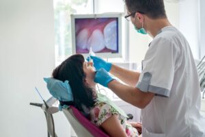 Radiologista realiza o procedimento de escaneamento intraoral. Ao fundo, é possível ver a visualização da arcada do paciente.